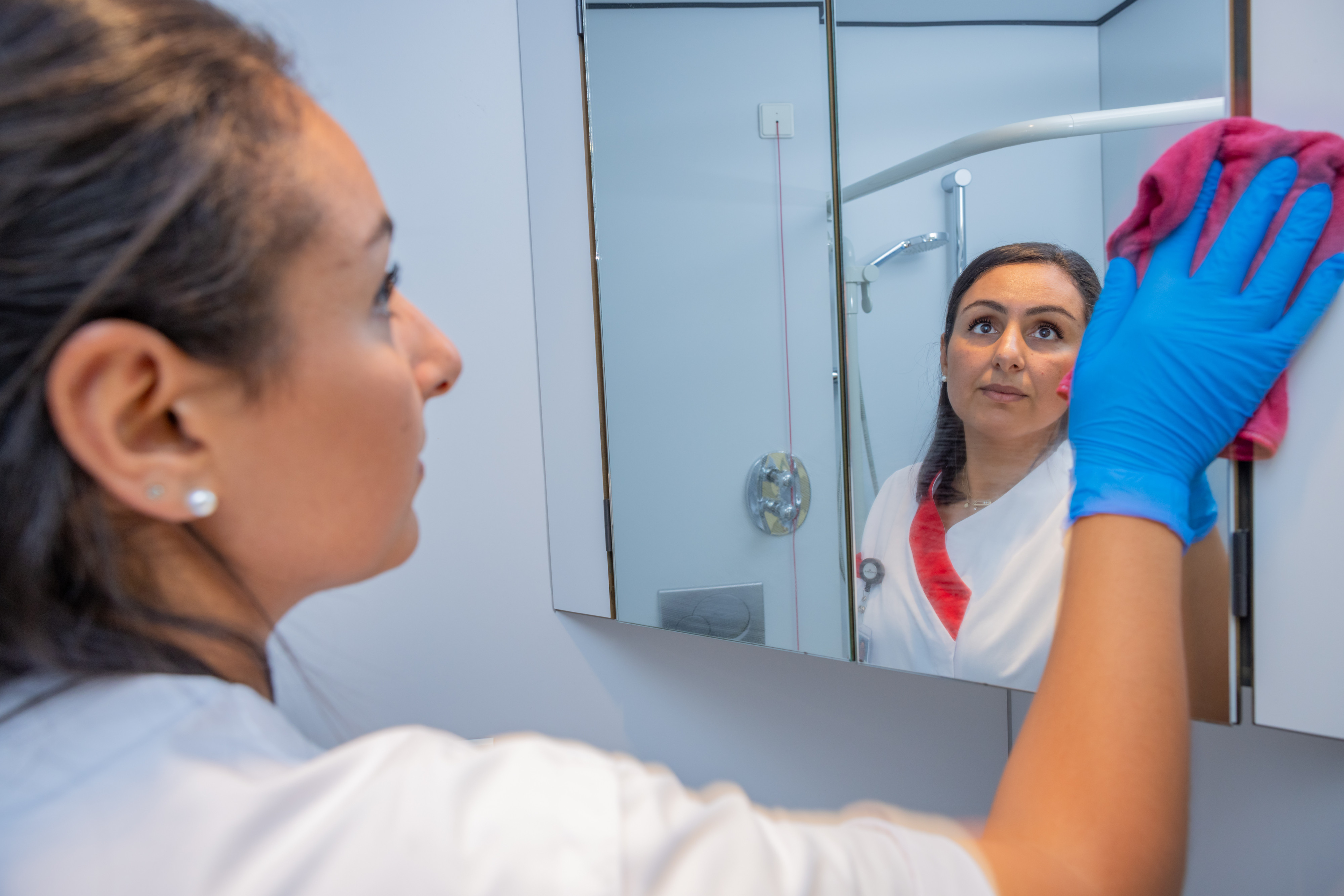 Schoonmaakster Sara kuist een spiegel in een ziekenhuiskamer